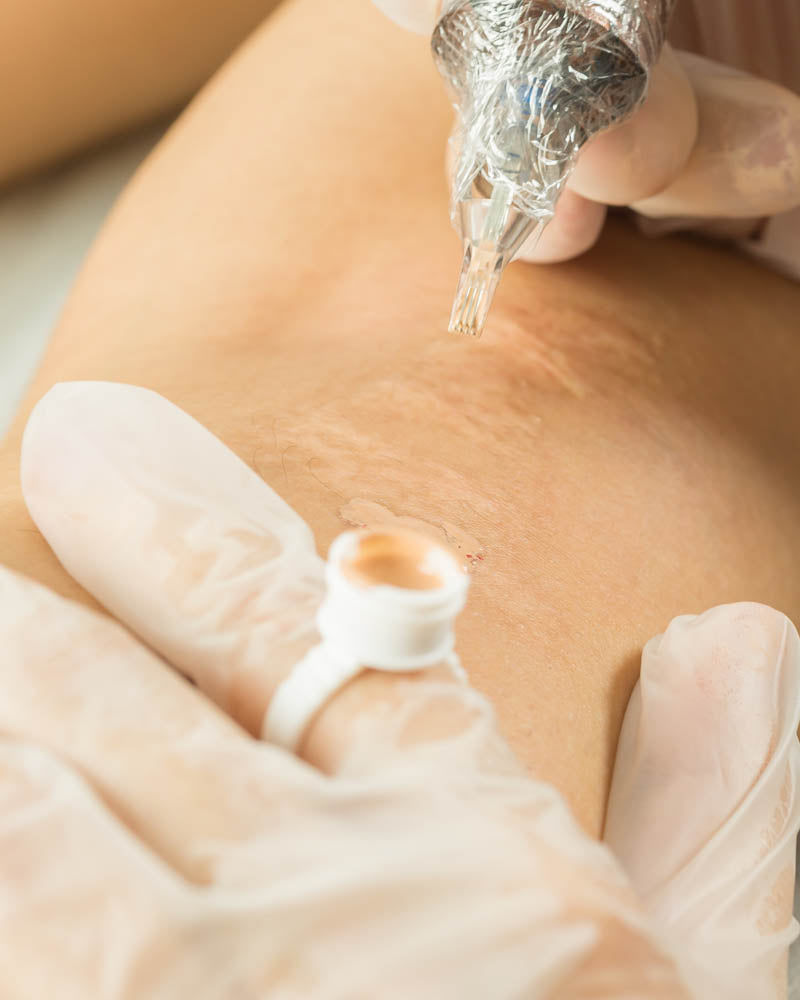 a close up of hands holding a needle with a pigment ring while tattooing over a section of skin