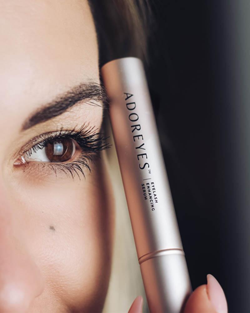 Close up of a woman holding Adoreyes Eyelash Serum beside her eye